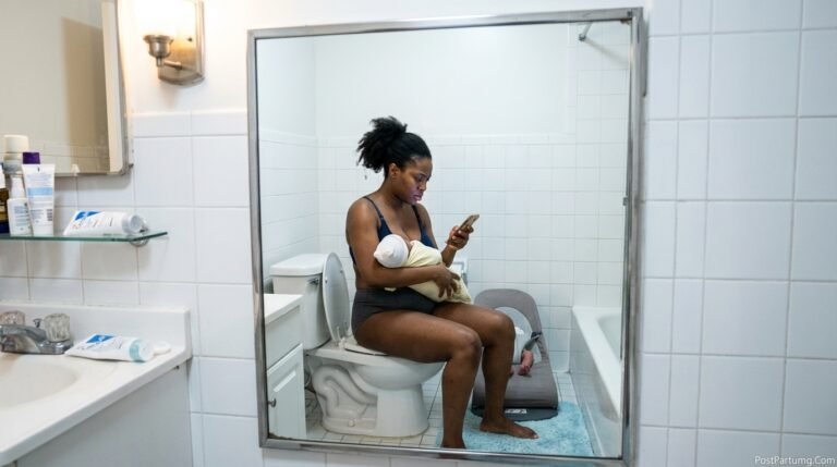 Breastfeeding mother sitting in discomfort from postpartum vaginal dryness symptoms reading about genitourinary syndrome of lactation on phone